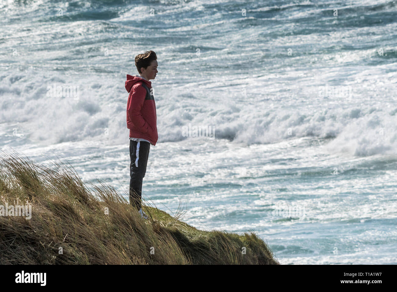 Un jeune adolescent debout sur la côte face à la mer. Banque D'Images