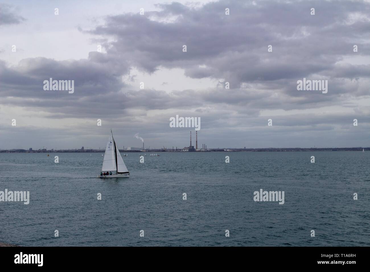 Un yacht de quitter le port de Dun Laoghaire avec les tours de la vieille Poolbeg Power Station et la nouvelle de Dublin i Banque D'Images