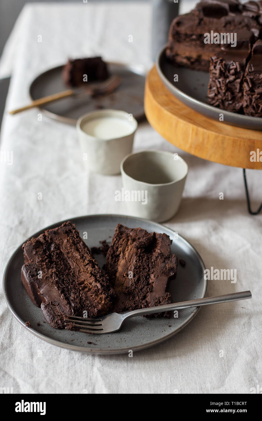 Morceaux de gâteau au chocolat sur la plaque grise, gâteau sur support en bois, verre de lait sur la table. Concept de dessert table set Banque D'Images Morceaux de gâteau au chocolat sur la plaque grise, gâteau sur support en bois, verre de lait sur la table. Concept de dessert table set Banque D'Images