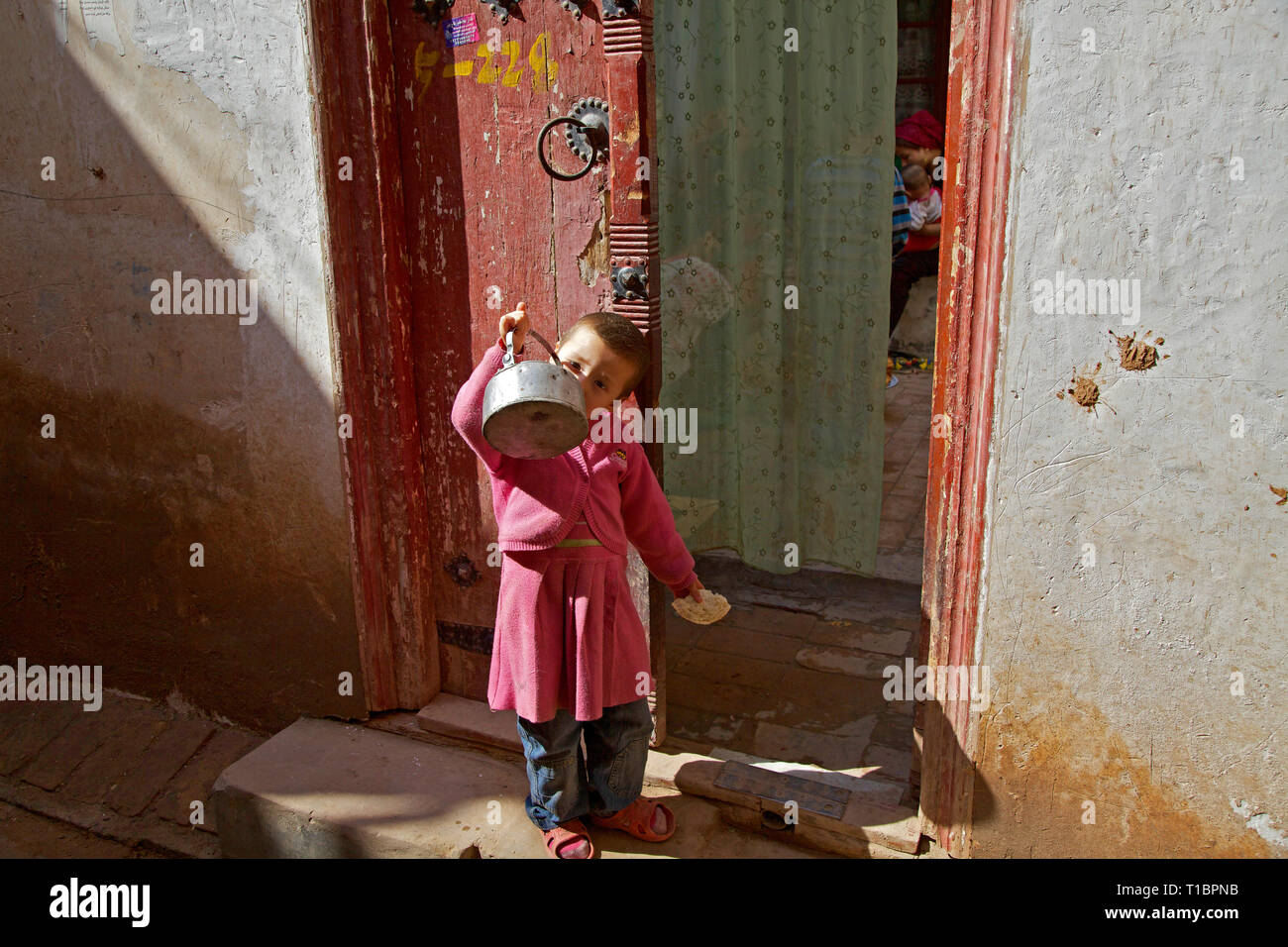 Petite Uighour enfant buvant de l'eau à l'extérieur de sa maison, vieille ville de Kashgar, région autonome du Xinjiang, Chine. Banque D'Images