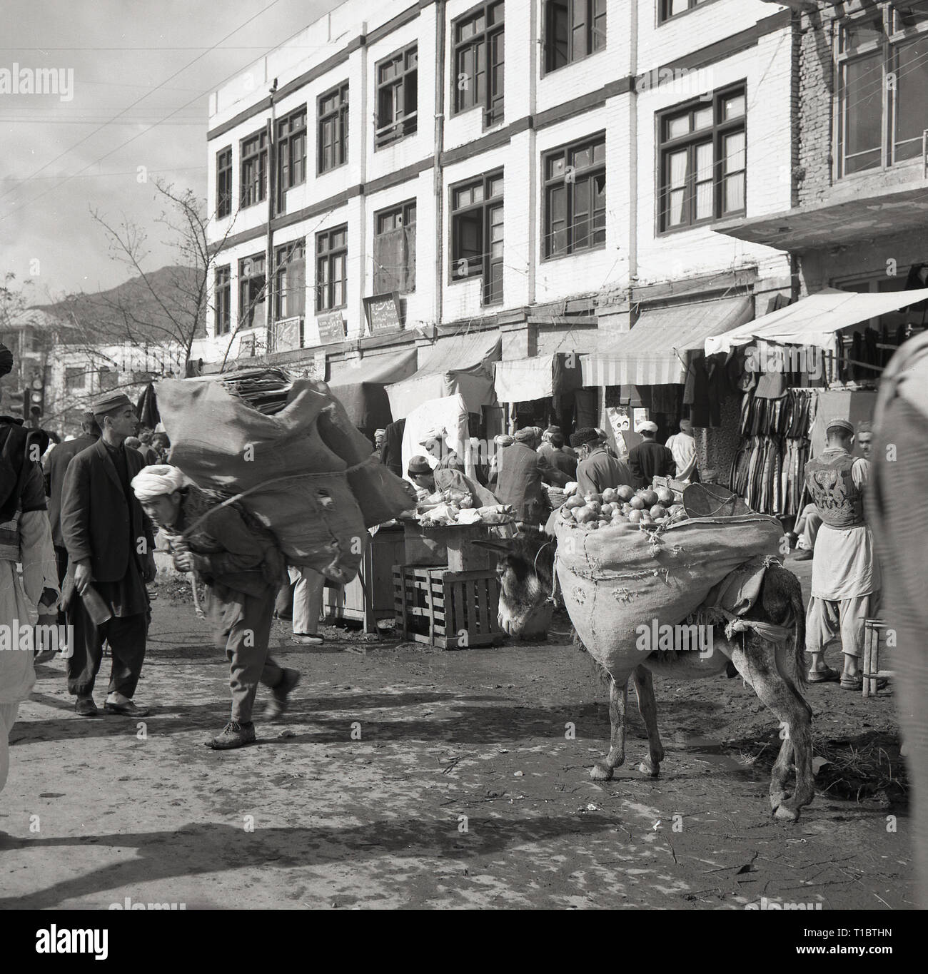 1960, Afghanistan, actiivty dans la capitale Kabal, vendeurs de rue et les stalles, avec un afghan homme transportant une lourde charge sur son dos. Banque D'Images