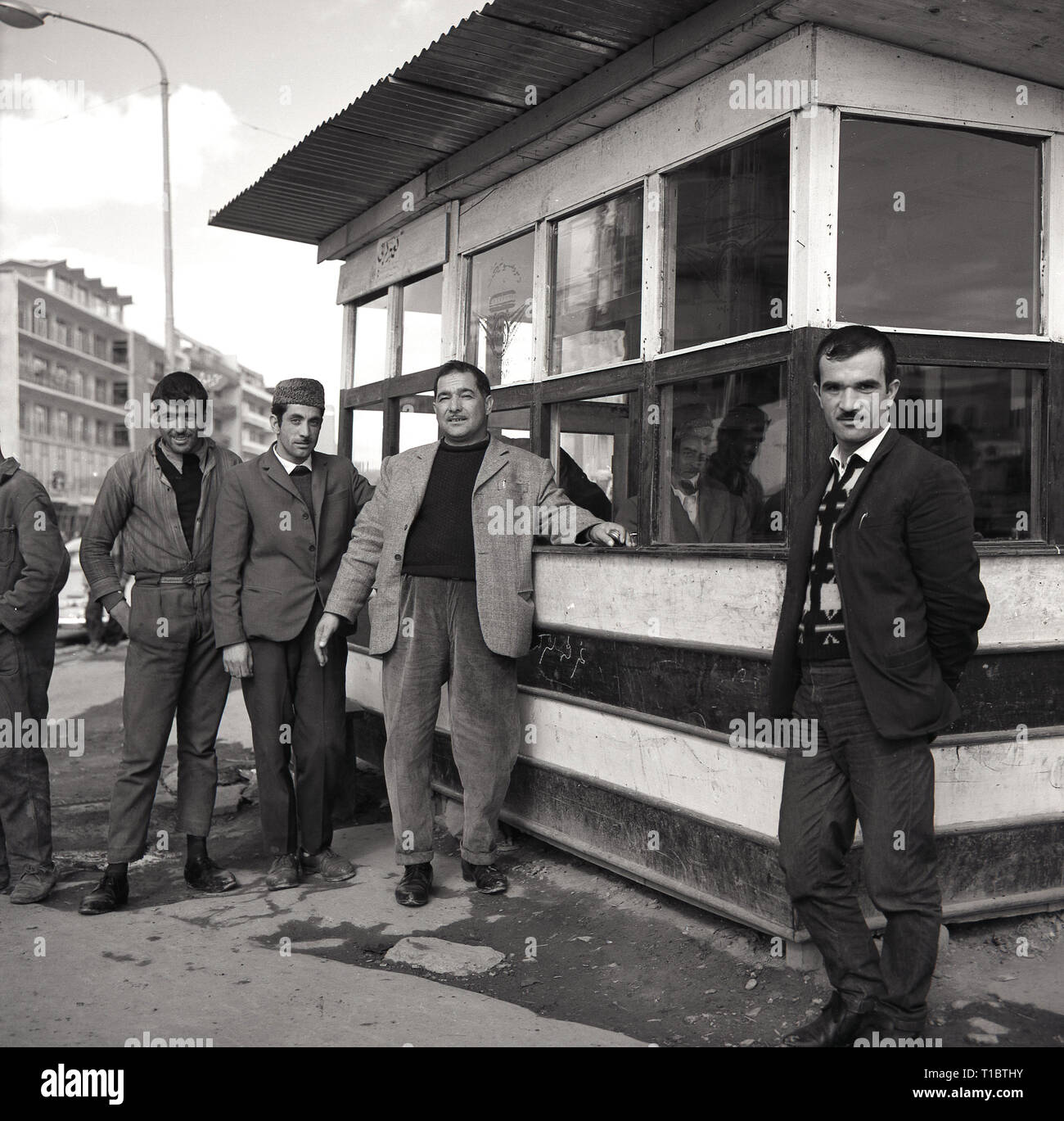 1960, Afghanistan, Kabal, quatre hommes se tenant debout à l'extérieur par des rues du centre-ville, avec des fenêtres et toit en tôle ondulée. Banque D'Images