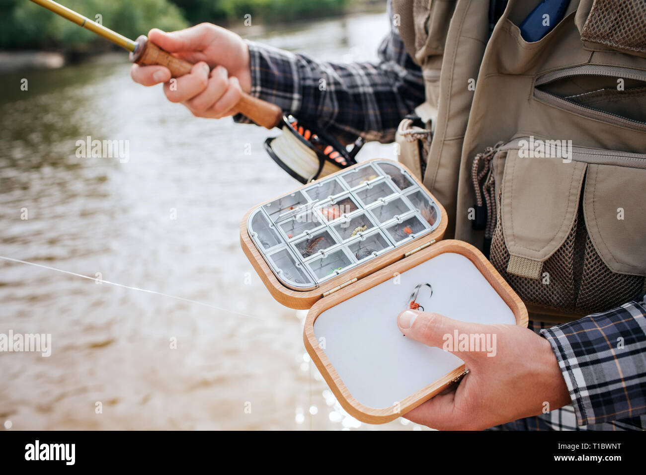 Close up de boîte en bois avec des plaques stratifiees usage silicone artificiel des mouches de pêche et appâts dans elle. L'homme la tient dans une main et a la tige dans l'autre Banque D'Images