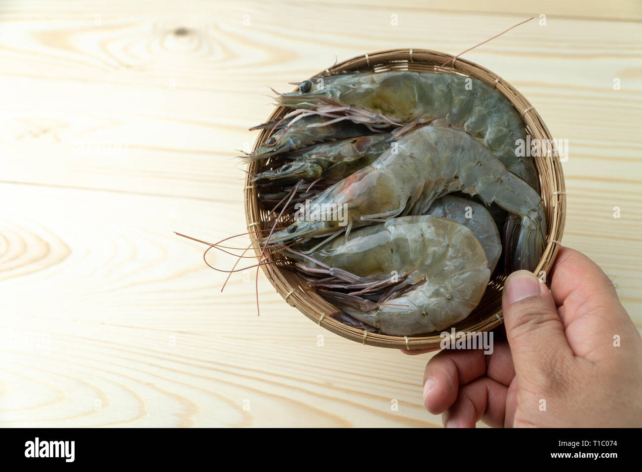 Les mains des hommes sont holding group de matières premières fraîches crevettes blanches du Pacifique en bambou bol sur table en bois. Banque D'Images