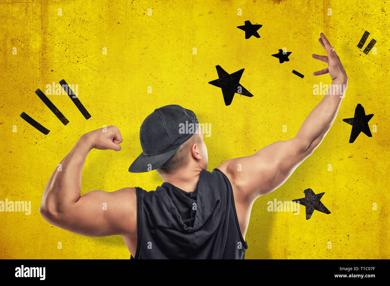 Strong muscular young man showing biceps avec black stars tirées sur fond de mur jaune Banque D'Images