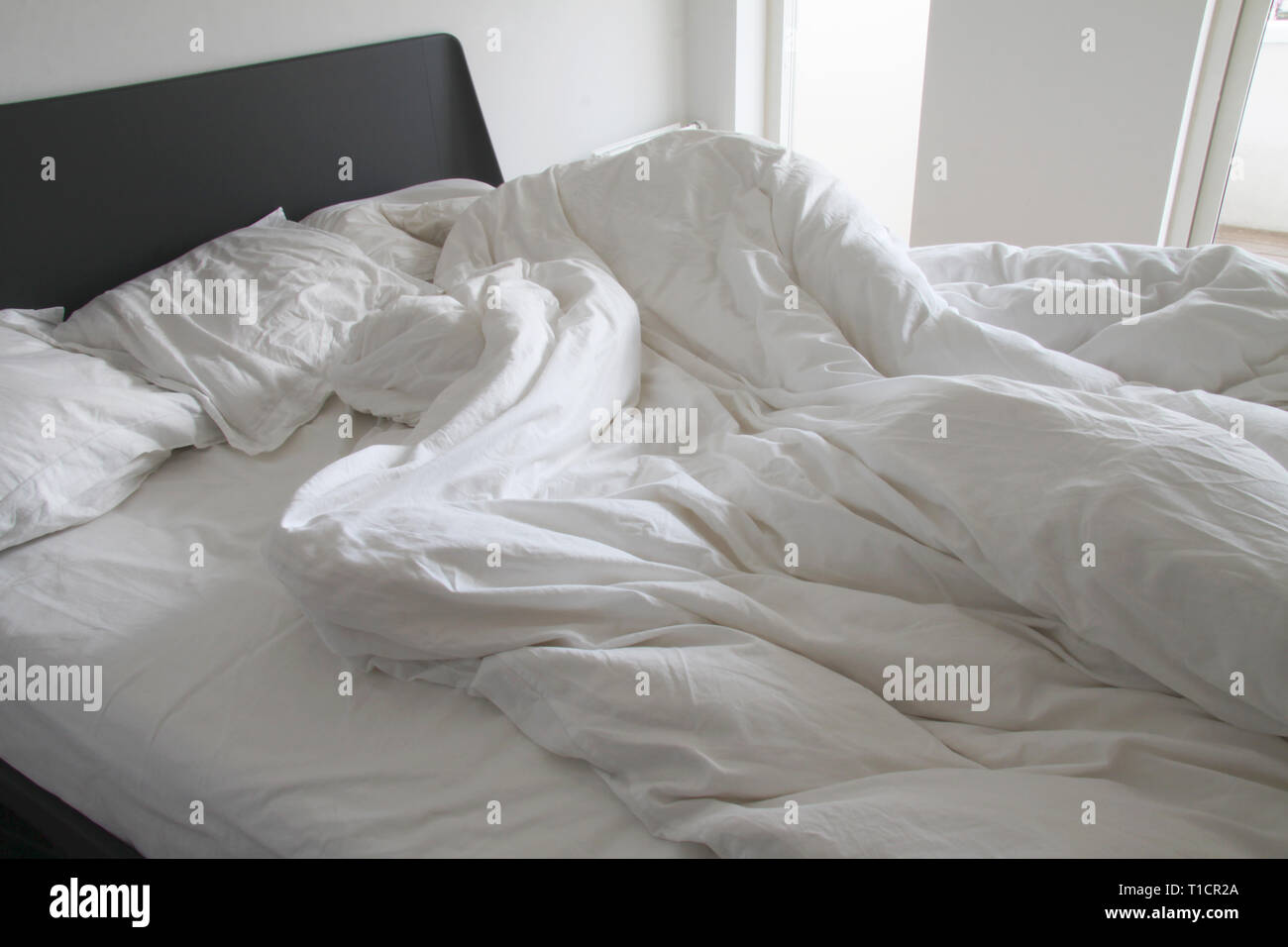 Messy blancs draps et oreillers de rides sur lit dans une chambre blanche Banque D'Images
