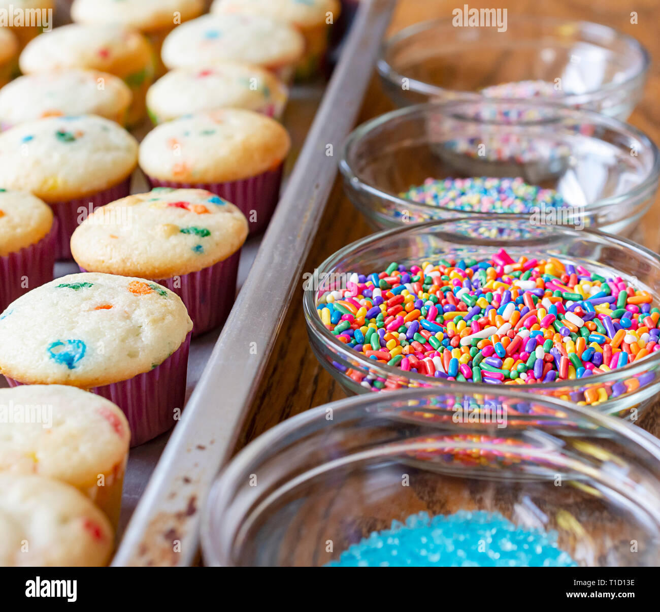 Rangée de candy sprinkles et des rangées de mini cupcakes en attente d'être givré. Banque D'Images