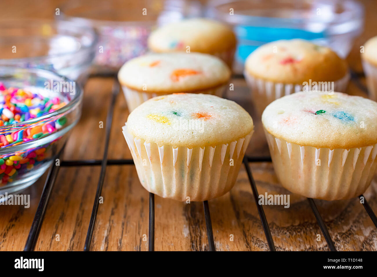 Mini cupcakes sur une grille en attente d'être givré. Divers sucres colorés et saupoudre de bols en verre autour de petits gâteaux. Banque D'Images