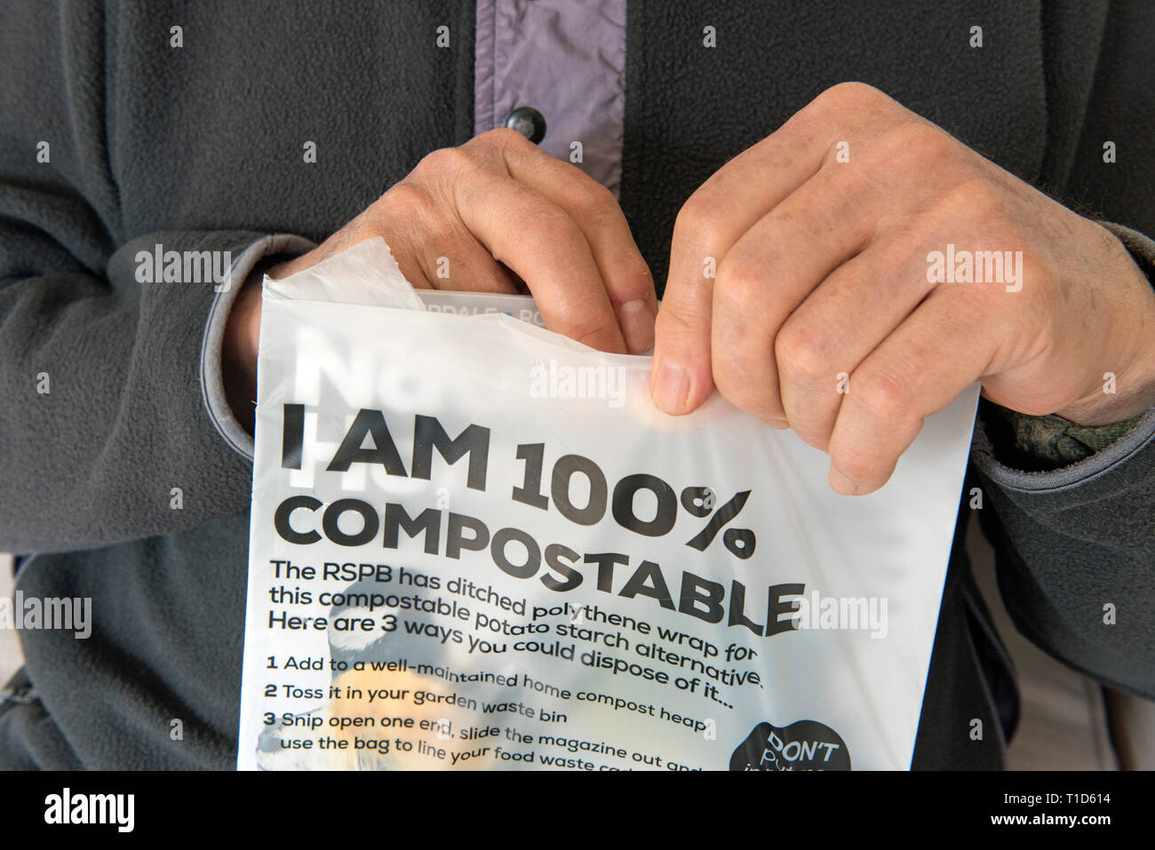 L'homme de l'ouverture du conditionnement de RSPB's magazine Nature's Home qui a un emballage compostable composé de fécule de pomme de terre, aucun déchet. Banque D'Images