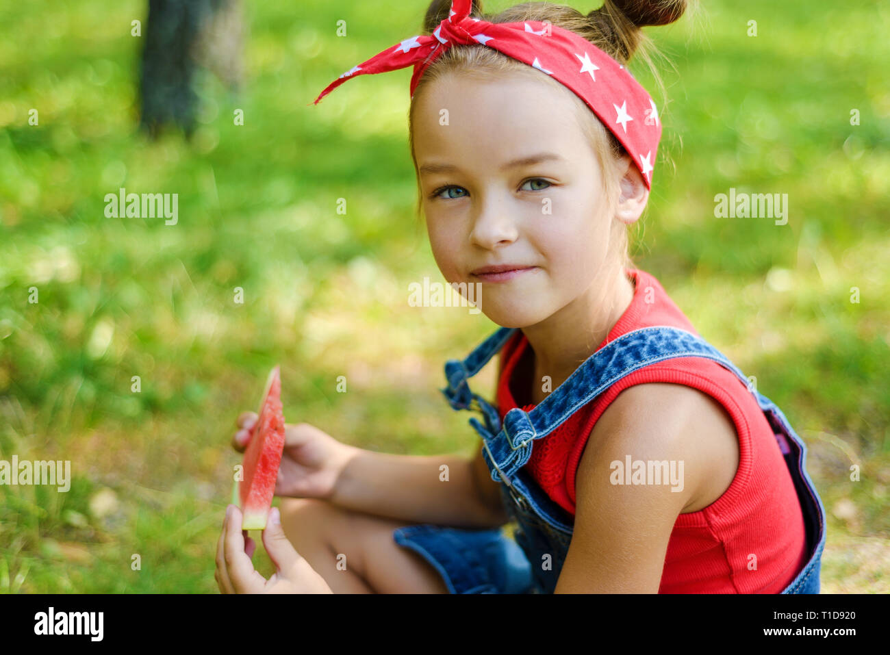 Portrait de petite fille en rouge T-shirt et salopette denim foulard en  tenant une pastèque mûre. l'enfant est assis sur l'herbe dans le parc Photo  Stock - Alamy