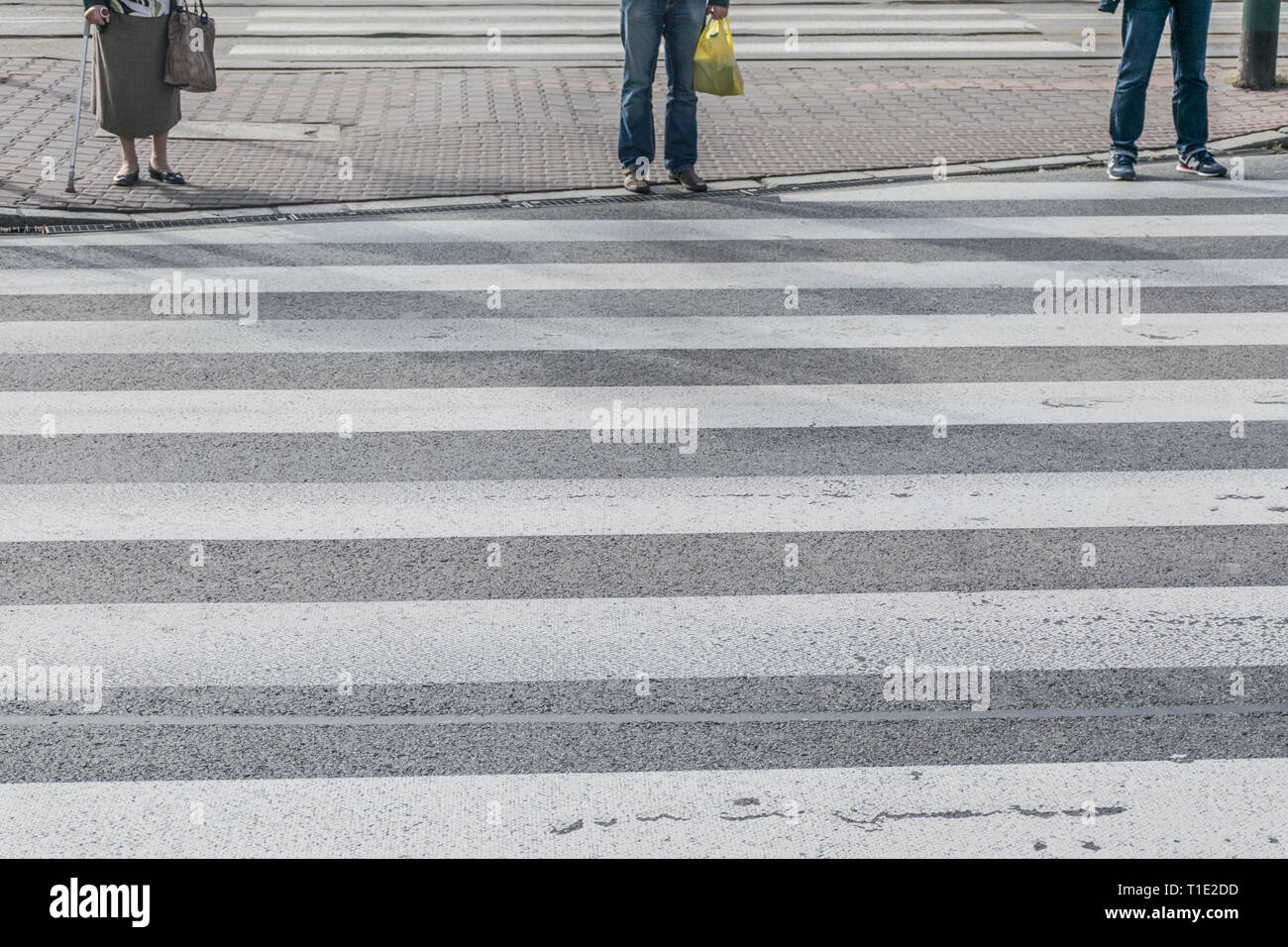 Les piétons attendent pour traverser sur la route, les pieds dans l'allée de circulation zebra Banque D'Images