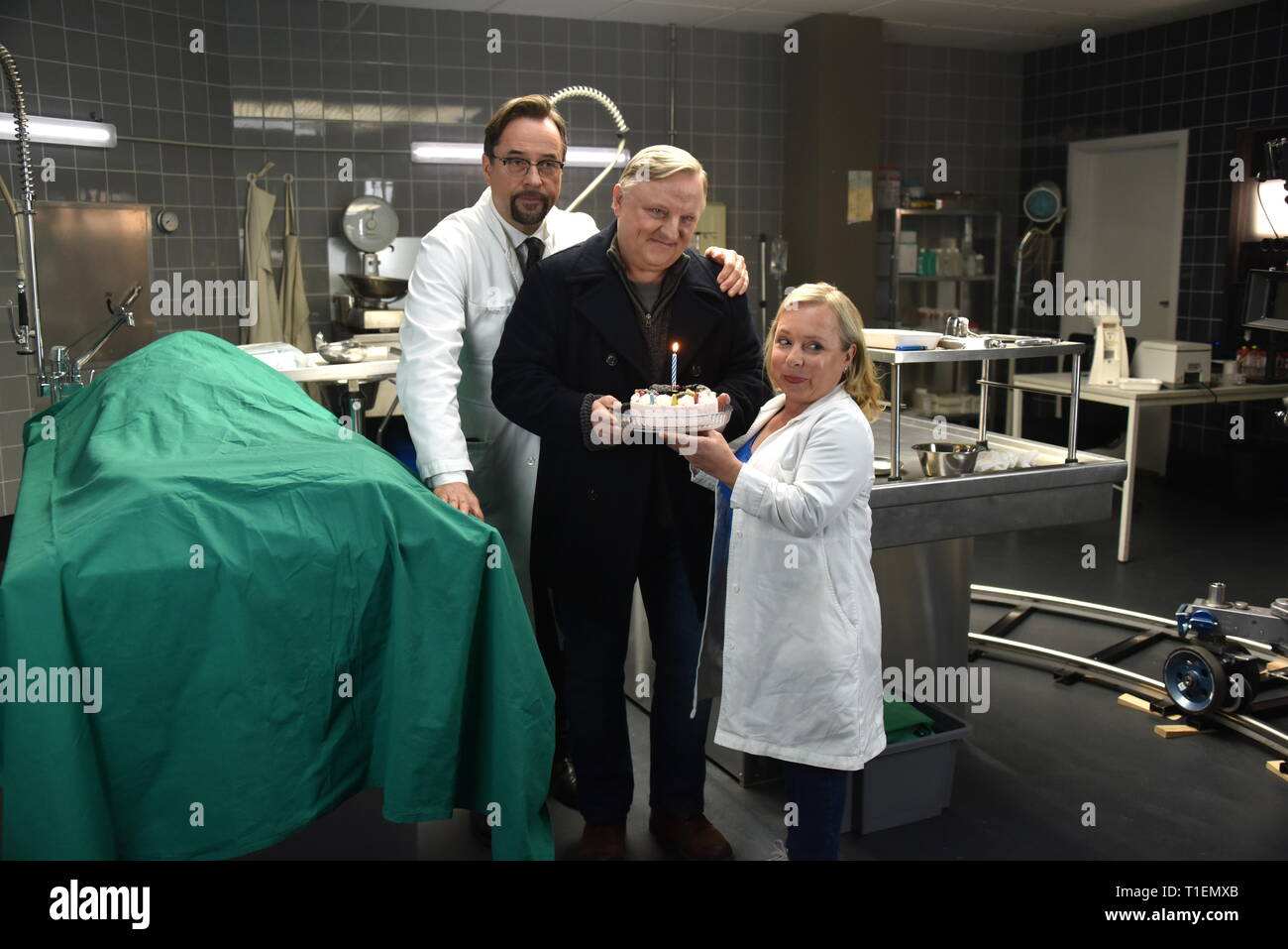 26 mars 2019, Berlin, Cologne : les acteurs Jan Josef Liefers (l-r), Axel Prahl et Christine Urspruch stand dans les décors de médecine légale pendant une séance photo au "Tatort Münster - Lakritz" (AT). Le gâteau a reçu offrent à l'occasion de son anniversaire. Photo : Horst Galuschka/dpa Banque D'Images