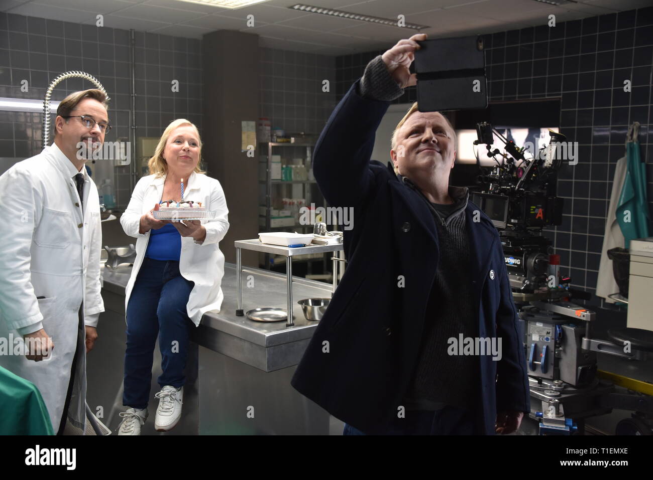 26 mars 2019, Berlin, Cologne : les acteurs Jan Josef Liefers (l-r), Axel Prahl et Christine Urspruch stand dans les décors de médecine légale pendant une séance photo au "Tatort Münster - Lakritz" (AT). Le gâteau a reçu offrent à l'occasion de son anniversaire. Photo : Horst Galuschka/dpa Banque D'Images