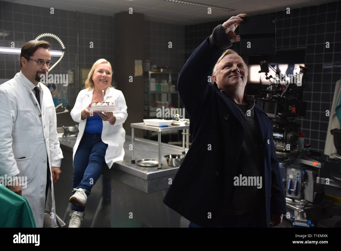 26 mars 2019, Berlin, Cologne : les acteurs Jan Josef Liefers (l-r), Axel Prahl et Christine Urspruch stand dans les décors de médecine légale pendant une séance photo au "Tatort Münster - Lakritz" (AT). Le gâteau a reçu offrent à l'occasion de son anniversaire. Photo : Horst Galuschka/dpa Banque D'Images