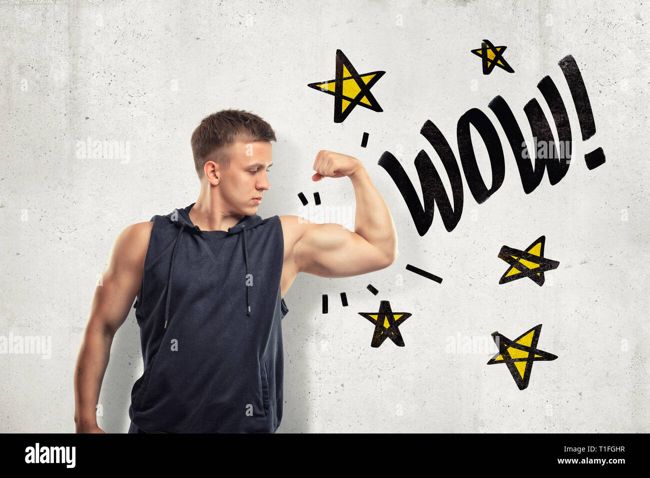 Strong muscular young man showing biceps avec WOW signer et jaune étoile dessiné sur fond de mur blanc Banque D'Images