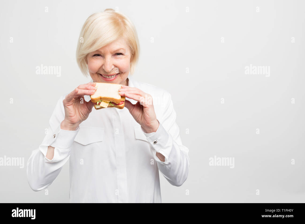 Femme aux cheveux blancs est debout et tenant un beau et bon morceau de sandwich. Elle n'a pas le temps de manger mieux repas. Se est avoir une saine alimentation il Banque D'Images