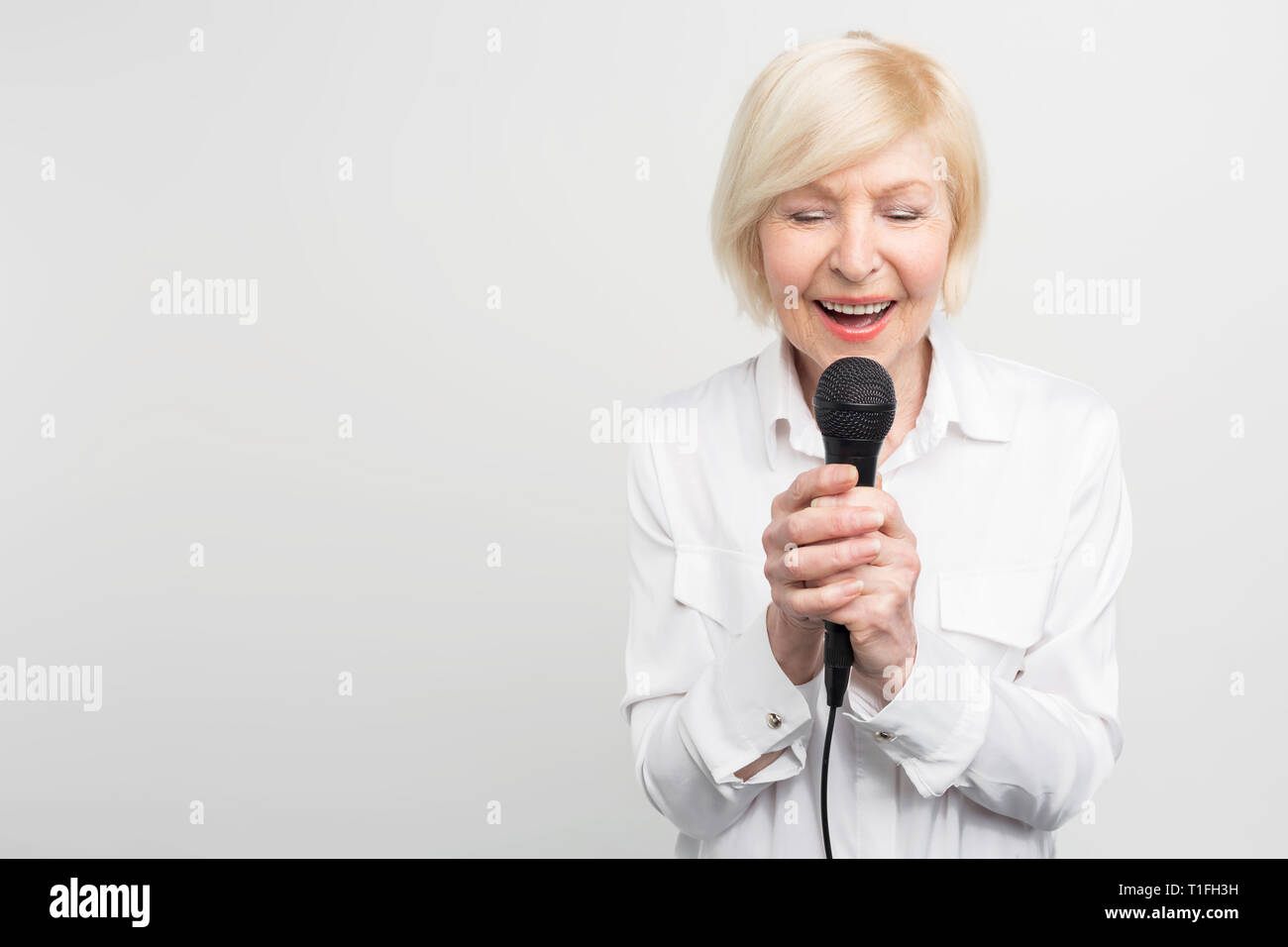 Belle et tendre photo de femme mature impressionnant chanter une chanson avec ses yeux fermés à l'aide d'un microphone. Isolé sur fond blanc. Banque D'Images
