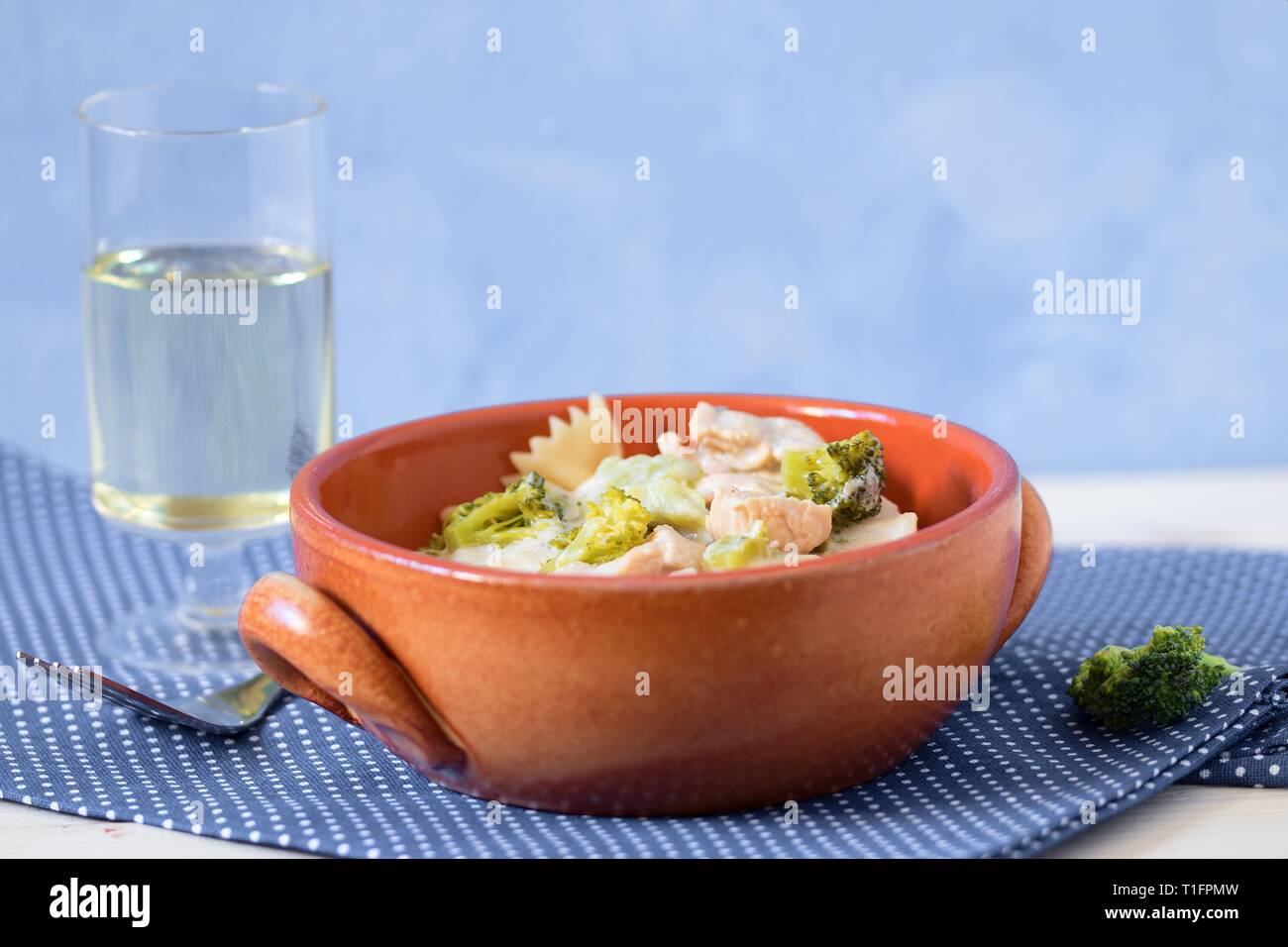 Les pâtes (farfalle) avec le brocoli, la viande de poulet et la crème dans un bol de faïence servi avec du vin blanc à pois sur tapis de table. Déjeuner simple sain Banque D'Images