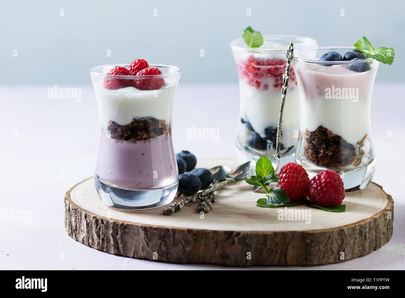 Weda de plusieurs grands verres avec les parfaits fruits des bois composé de yaourts, céréales, bleuets et framboises sur disque en bois Banque D'Images