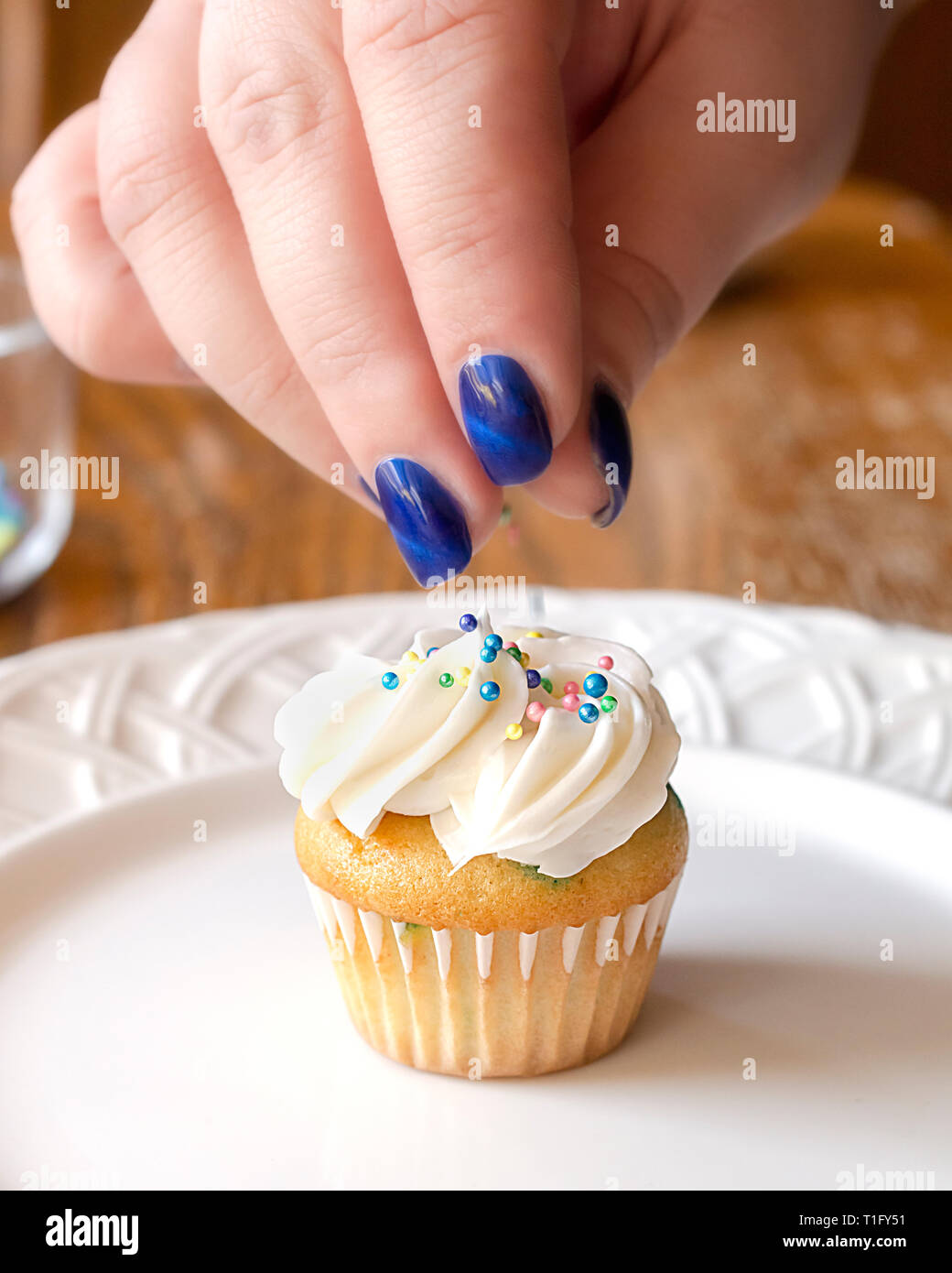 Tomber sur un sprinkles couleurs pastel givré fraîchement mini cupcake. La main seulement. Banque D'Images