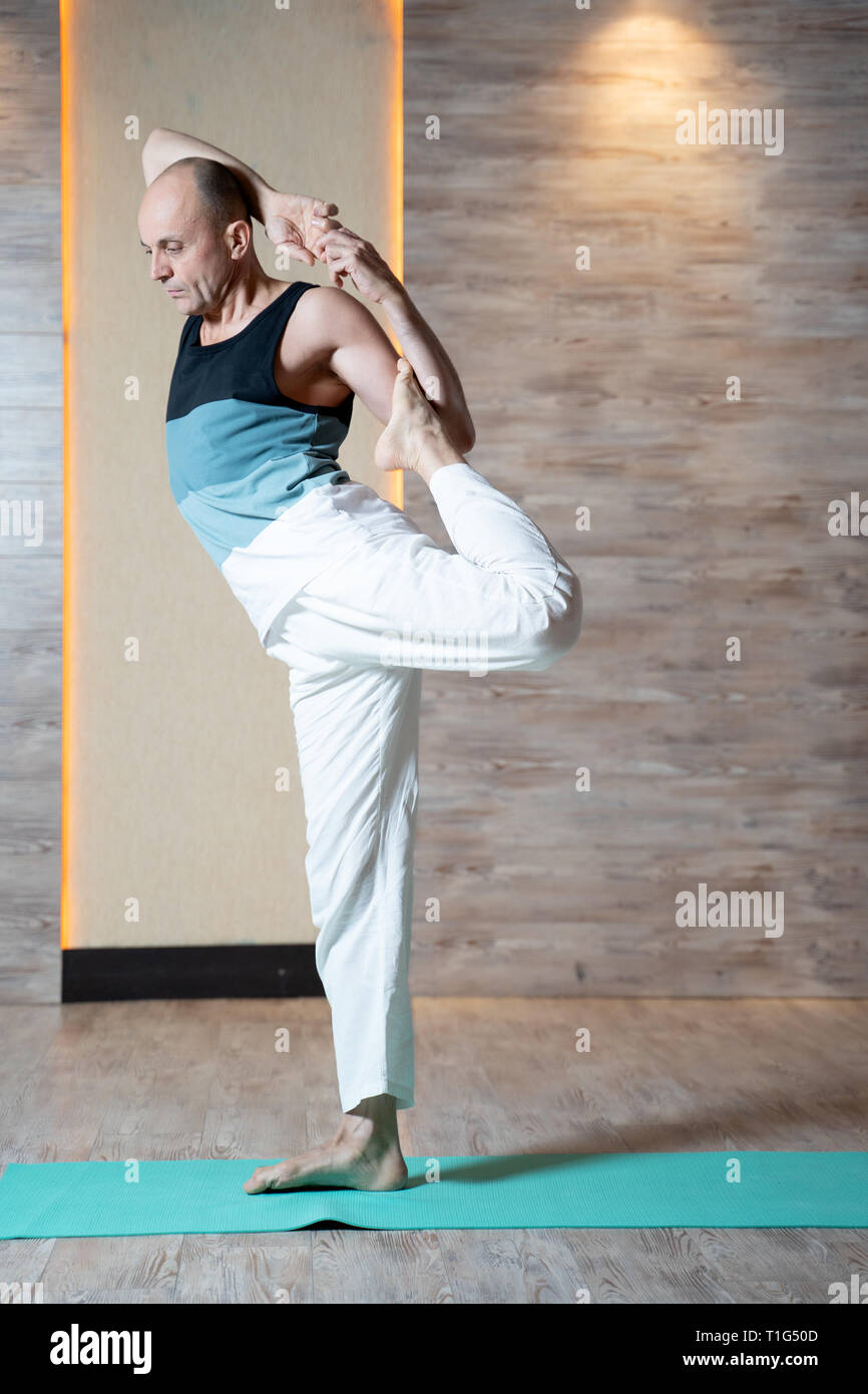 Homme debout jambe faisant du yoga sur le tapis bleu. Banque D'Images