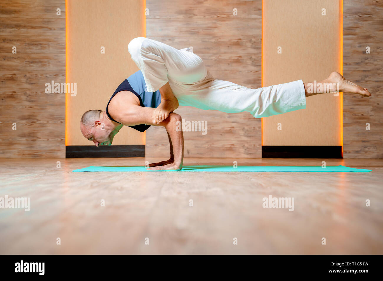 Homme debout sur les trains yogi une part sur un tapis bleu. Banque D'Images