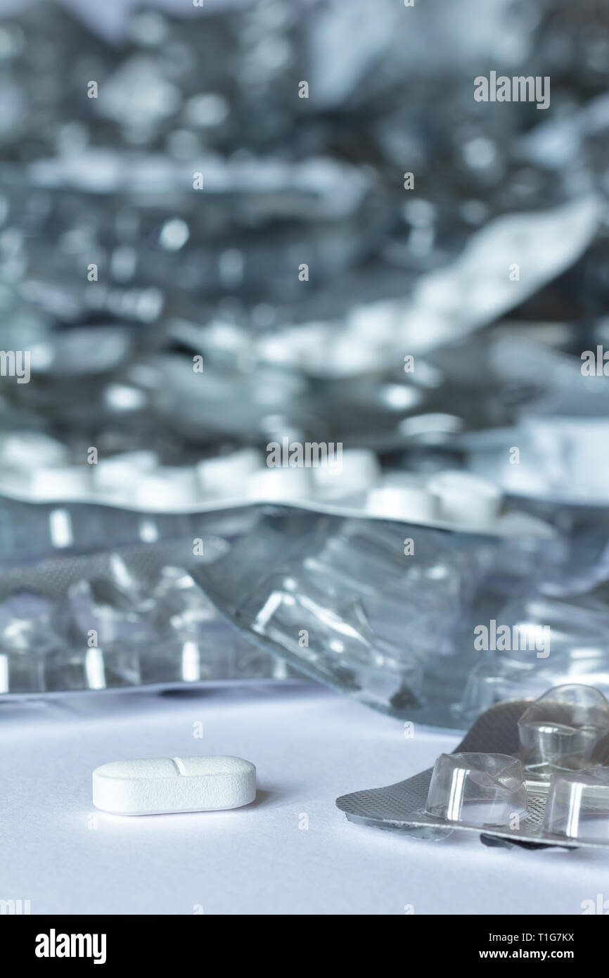 Un seul comprimé en face d'un grand nombre de blisters vides sur fond blanc, concept de l'abus de drogues Banque D'Images