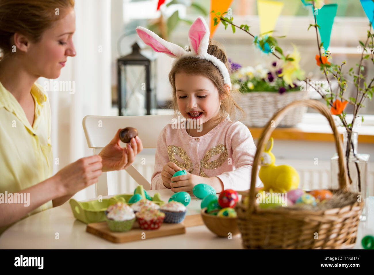 Mère et fille célébrer Pâques, manger des œufs en chocolat. Maison de famille heureuse. Cute little girl avec drôle de visage en oreilles de lapin en riant, smiling Banque D'Images