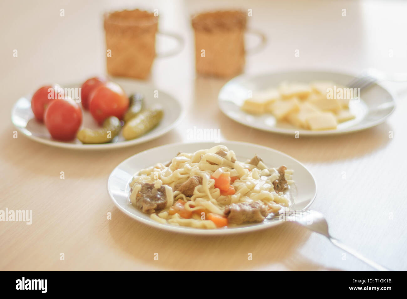 Des pâtes avec des tranches de viande et les carottes. Tomates Marinées et les concombres. Tranches de fromage dans une assiette. Deux tasses sur la table. Banque D'Images