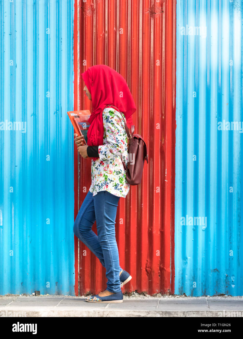 Male, Maldives - Février 11th, 2019 : A female student wearing hijab marcher sur un panneau mural en carton ondulé à Malé, Maldives. Banque D'Images