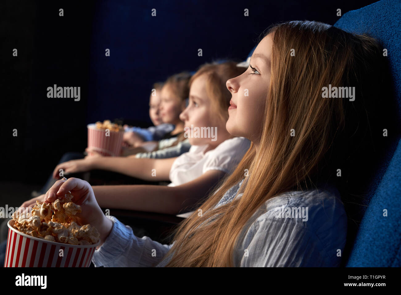 Les enfants assis dans de confortables fauteuils de cinéma, regarder attentivement film ou dessin animé. Beautiful Girl holding seau de maîs éclaté, bénéficiant d film premiere. Banque D'Images