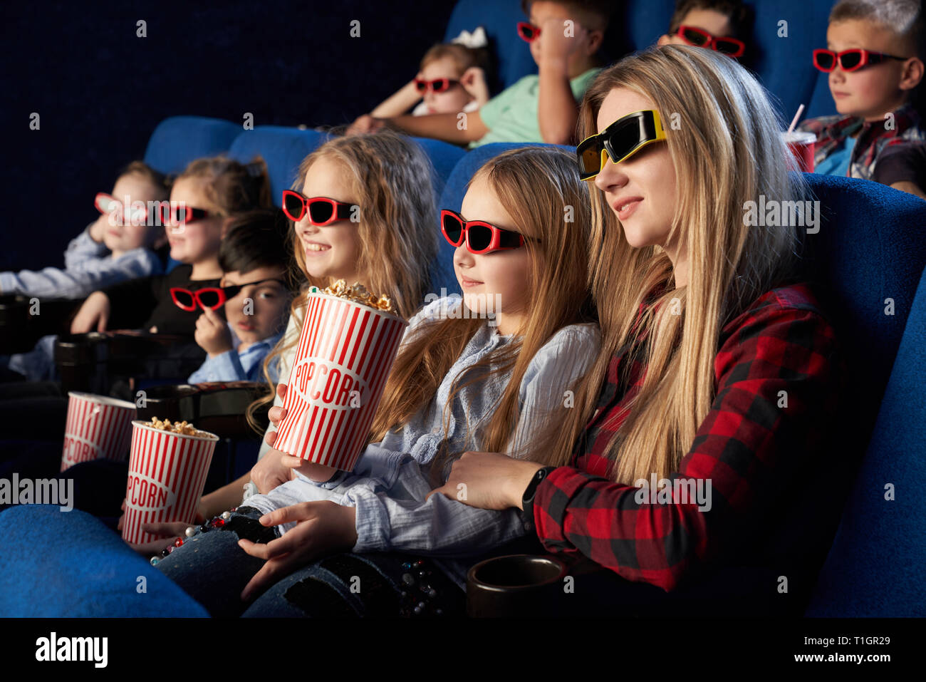 Mère et fille assis ensemble dans un cinéma, bénéficiant d première de film. Les enfants portant des lunettes 3D en regardant des film, holding popcorn des seaux. Banque D'Images