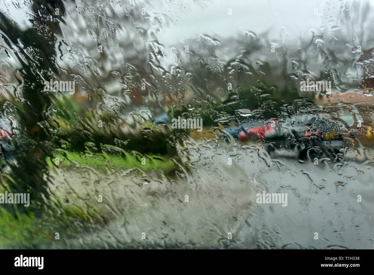 La pluie sur les pare-brise de voiture du flou rue résidentielle de banlieue en arrière-plan. Banque D'Images