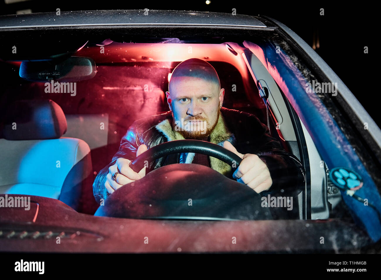 Conducteur dans une veste en cuir dans la voiture dans l'obscurité. Séance photo de nuit Banque D'Images