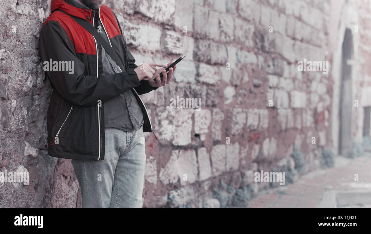 Jeune homme debout contre un mur et l'arrière-plan en utilisant votre smartphone. La technologie et le style de concept. Banque D'Images