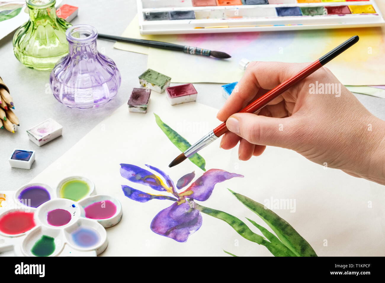 Painter holding un pinceau dans sa main. Aquarelle Dessin - Iris flower et artistique sur l'équipement de bureau. Vue d'en haut. Dessin peintre à lieu de travail. Banque D'Images