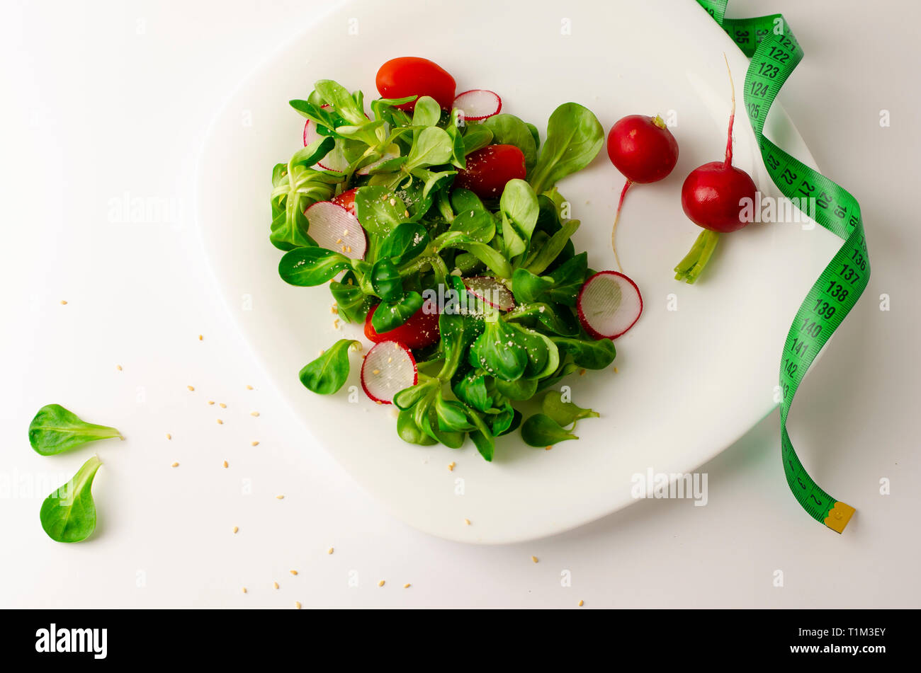 Salade de légumes frais de radis, tomates et salade de maïs ou Valerianella locusta. Close up sur plaque blanche et ruban à mesurer. Régime, la perte de poids Banque D'Images