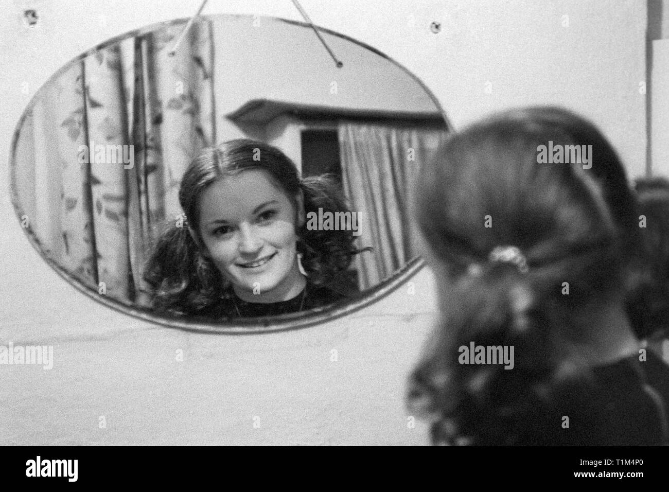 Jeune fille avec des nattes souriant à son reflet dans un vieux miroir mural style années 60, Hongrie Banque D'Images