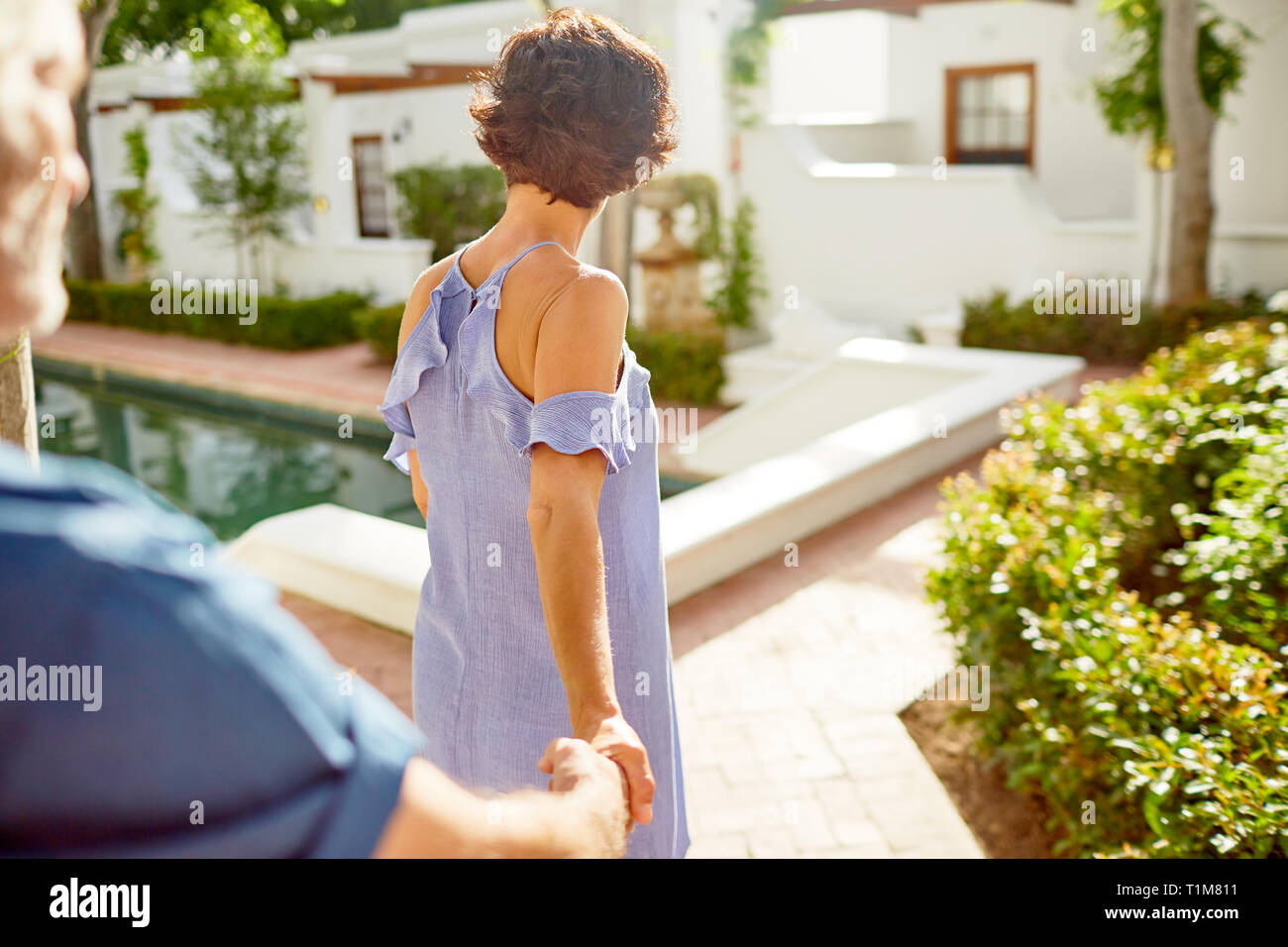 Couple Holding Hands, marche à pied à la piscine ensoleillée Banque D'Images