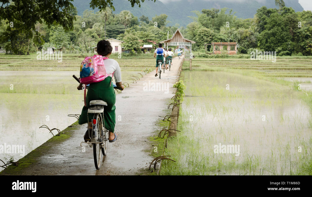 L'HPA, LE MYANMAR - 13 juin 2014 : Des enfants en uniforme d'faire de la bicyclette sur un pont en béton à travers les rizières, autour d'une ville du sud de l'HPA Banque D'Images