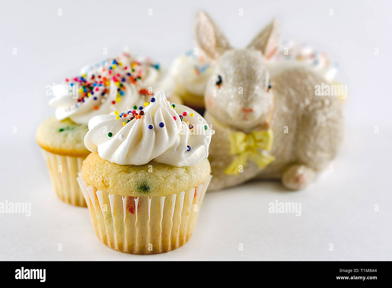Confettis blanc cake mini cupcake de près. Cupcakes supplémentaires en arrière-plan flou avec lapin de Pâques. Fond blanc avec des cultures horizontales. Banque D'Images