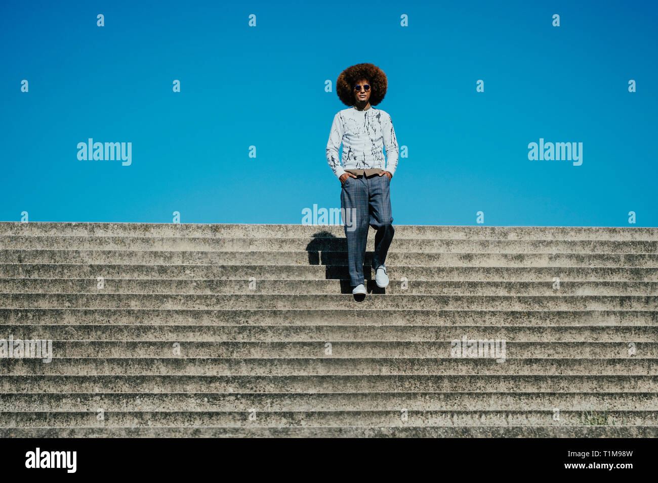 Portrait confiant, cool jeune homme avec afro sur des marches ensoleillées Banque D'Images