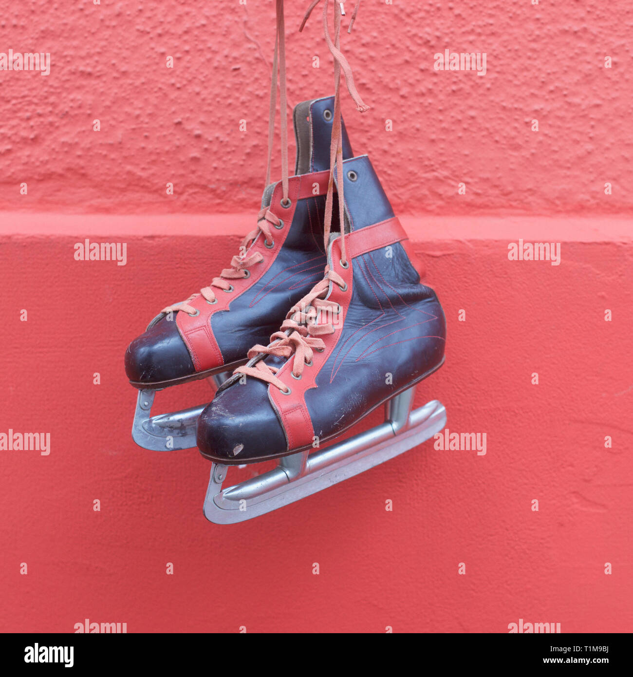 Patins à glace accroché contre mur rouge Banque D'Images