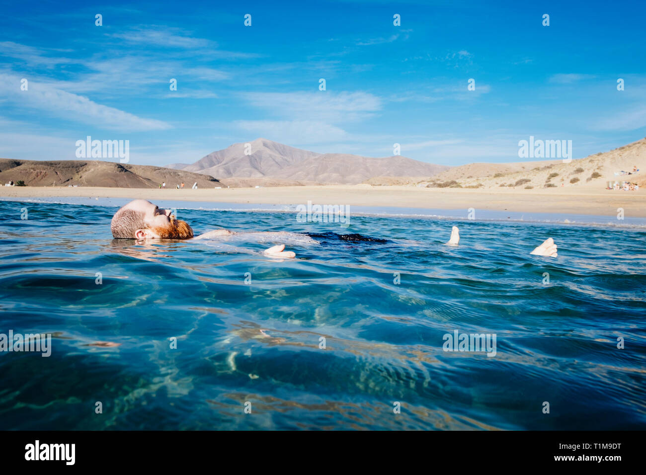 Homme insouciant flottant dans l'eau bleue de l'océan, plage de Papagayo, Lanzarote, îles Canaries, Espagne Banque D'Images