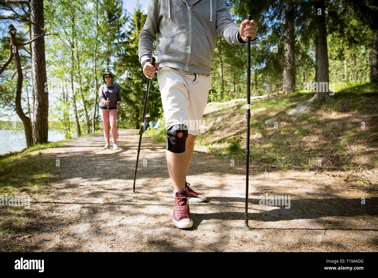 Homme avec pansement sur le genou. Sport de réadaptation en Finlande - la marche nordique. Homme et femme mature randonnées en vert forêt ensoleillée. Les personnes actives à l'extérieur. Banque D'Images