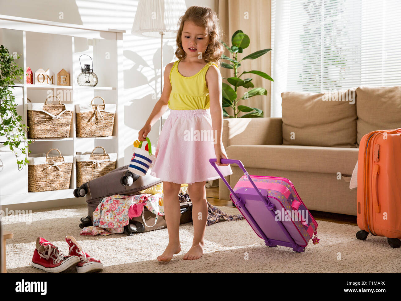 Heureuse petite fille assise dans la salle de séjour à la maison, soigneusement l'emballage des vêtements d'été colorés et des jouets en assurance valise pour un nouveau voyage. T de l'enfant Banque D'Images