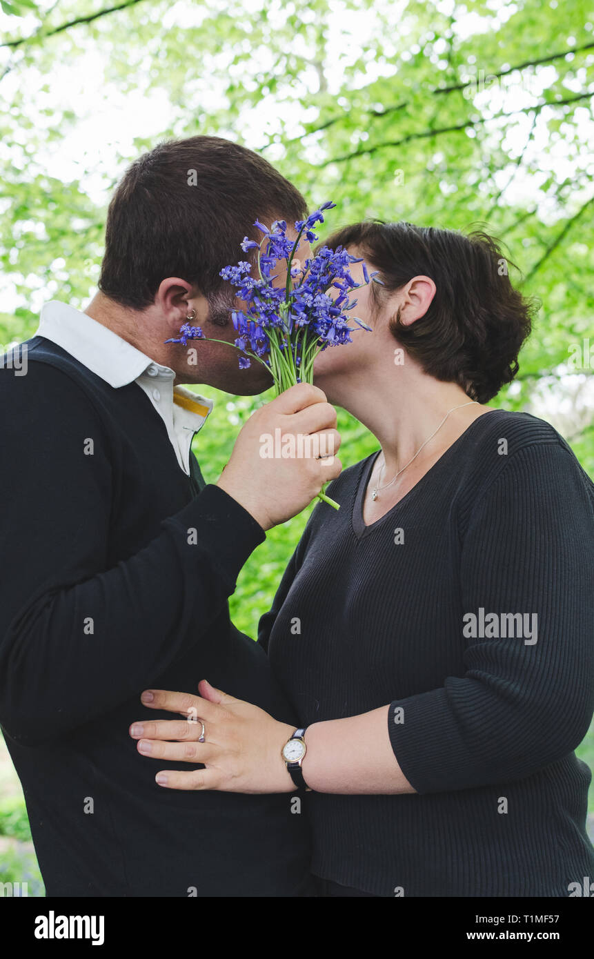 Couple in love se cacher derrière bluebell flowers s'embrassant. Banque D'Images