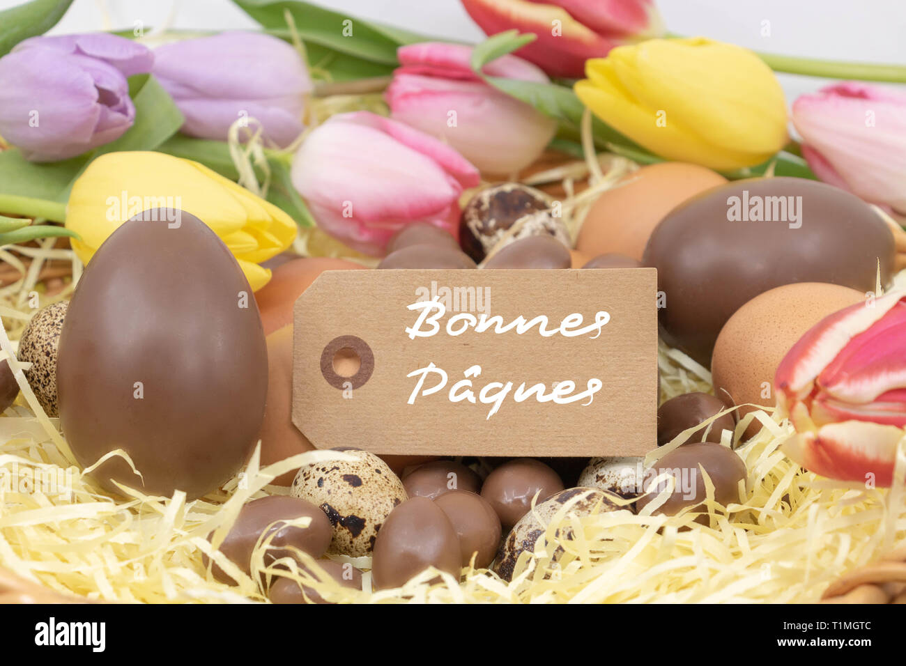 Joyeuses pâques (bonnes Pâques Joyeuses Pâques est écrit en français) sur une étiquette, célébration de Pâques avec des œufs en chocolat et de tulipes pastel Banque D'Images