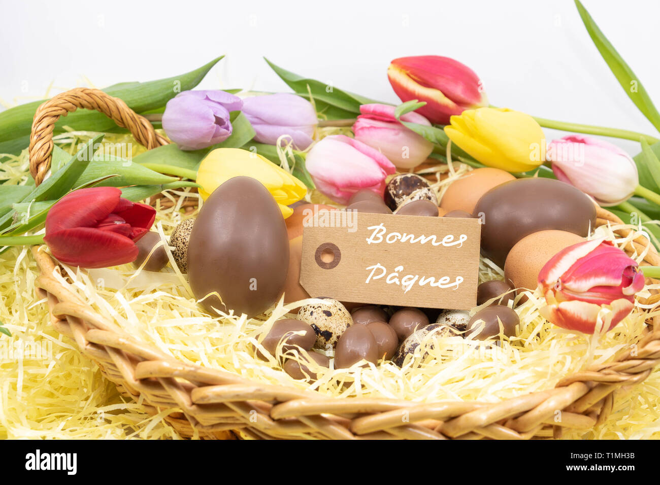 Joyeuses Pâques (bonnes Pâques Joyeuses Pâques est rédigé en français) sur une étiquette entouré de tulipes pastel et différents oeufs de Pâques Banque D'Images