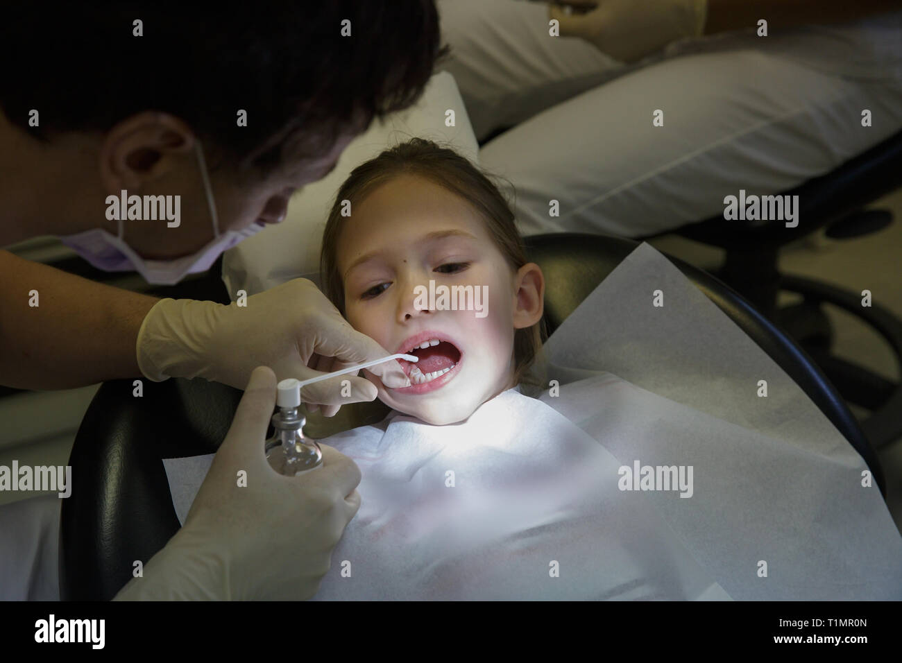 Petite fille au bureau de dentiste, un dentiste l'application de l'antiseptique pour les traitements dentaires. Les soins dentaires pédiatriques concept. Banque D'Images